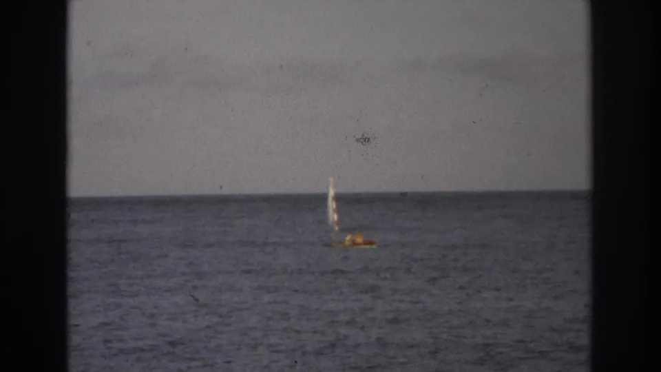 A small sailboat, possibly with occupants visible only as tiny shapes, crosses calm water near Ocean City, New Jersey in 1968 footage.