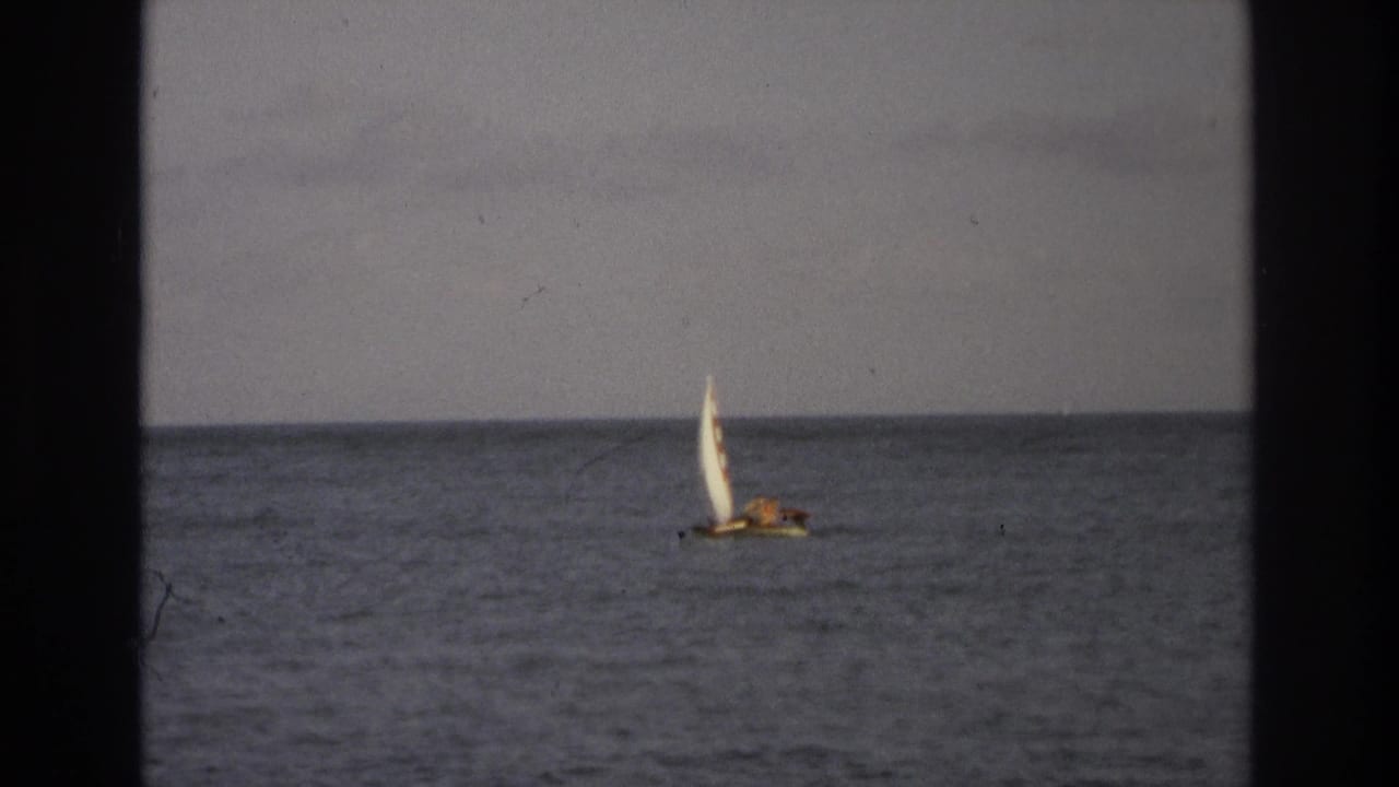 Small white-sailed boat on a gray ocean, framed by dark 8mm film borders.