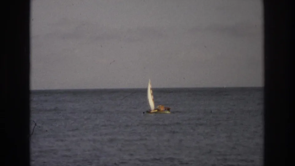 A small sailboat with a white sail crosses the ocean off Ocean City, New Jersey in 1968 home-movie footage.