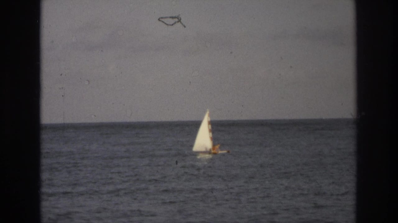 White sailboat farther right on open water beneath a muted sky.