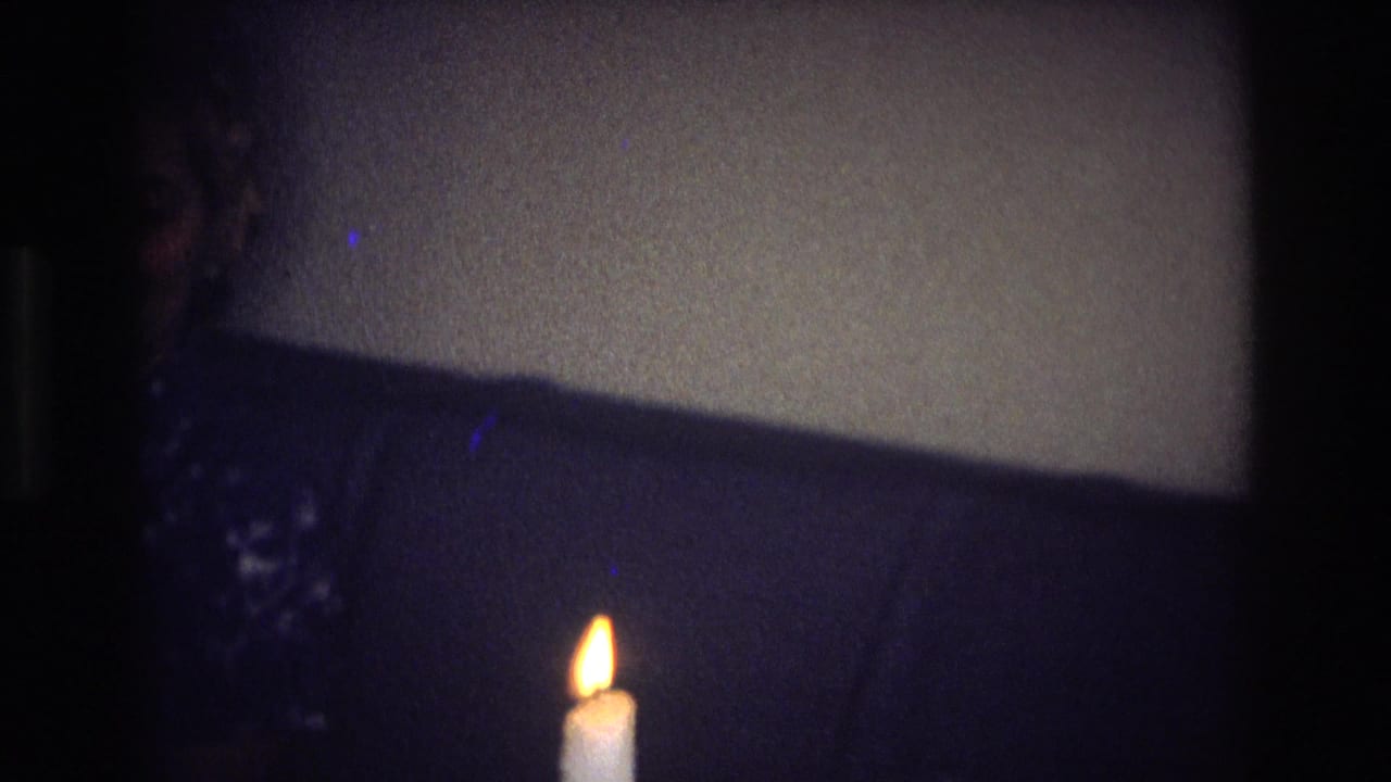 Single lit candle against a dim wall and dark couch area.
