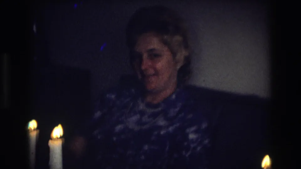 A smiling adult woman sits behind multiple lit candles on a dark couch in the 1968 Ocean City, New Jersey home-movie clip.