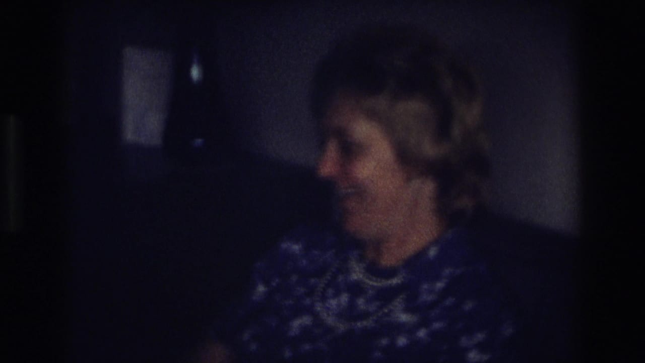 Older woman in the 1968 Ocean City home movie turns sideways and smiles, with her pearl necklace visible against a blue patterned dress.