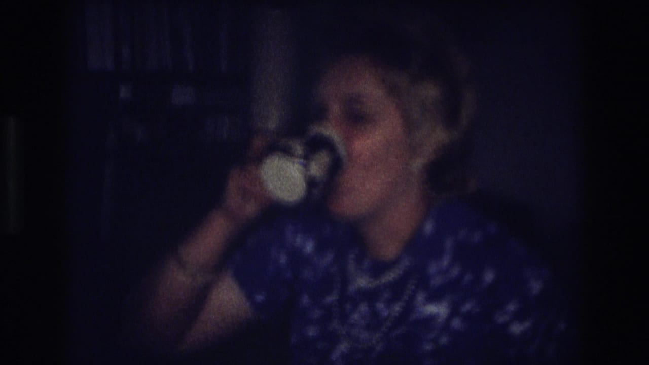 In a 1968 Ocean City, New Jersey home-movie frame, a woman in a blue patterned dress sips from a white cup in a dim interior.