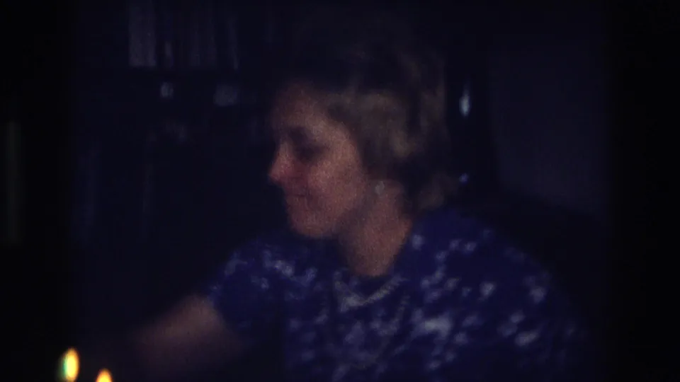 The woman sits turned to the side in a dark 1968 Ocean City interior, with small candle flames visible near the lower edge.