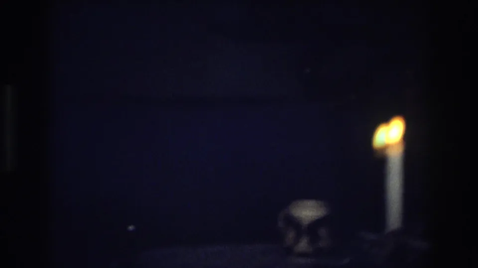 A candle burns at the edge of a dark tabletop in the 1968 Ocean City home-movie scene, with a small object nearby.