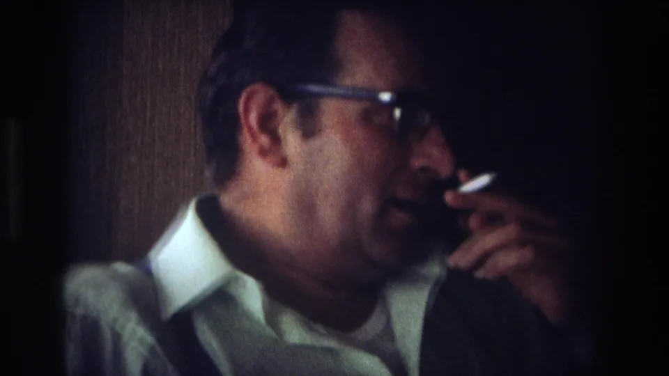 1968 Ocean City home-movie frame of a man in glasses smoking a cigarette in a dim interior.