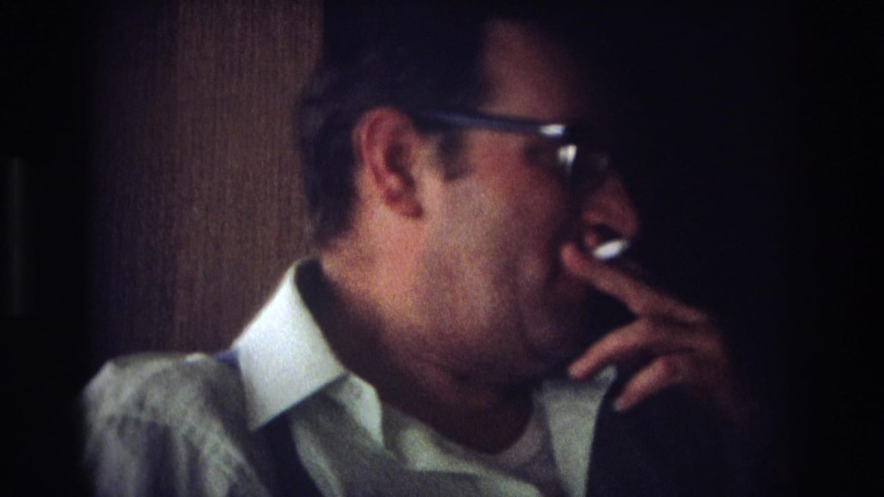 In 1968 Ocean City home-movie footage, a man in dark-framed glasses and a collared shirt holds a cigarette near his mouth indoors.