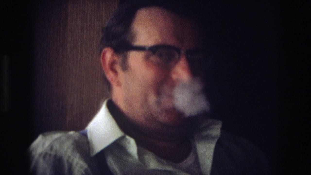 Man in glasses exhales smoke while seated indoors.
