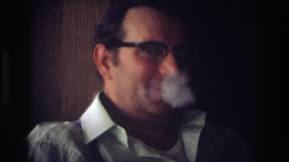 A man in glasses exhales visible smoke in a dim indoor setting in this 1968 Ocean City, New Jersey home-movie frame.