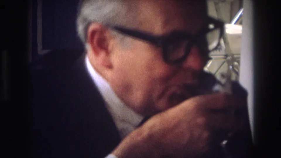 An older man in dark glasses and a suit jacket raises a small glass near his mouth in 1968 Ocean City home-movie footage.