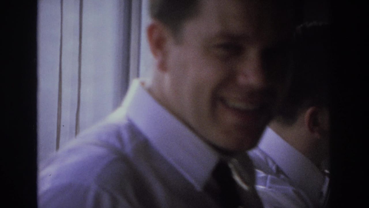 In 1968 Ocean City home-movie footage, a smiling adult man in a white shirt and dark tie stands close to the camera in a dim private interior.