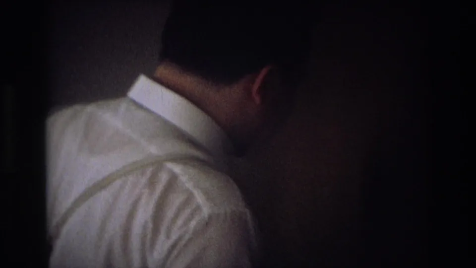 The man is seen from behind in a white shirt as he faces a darker doorway or closet area inside the private interior.