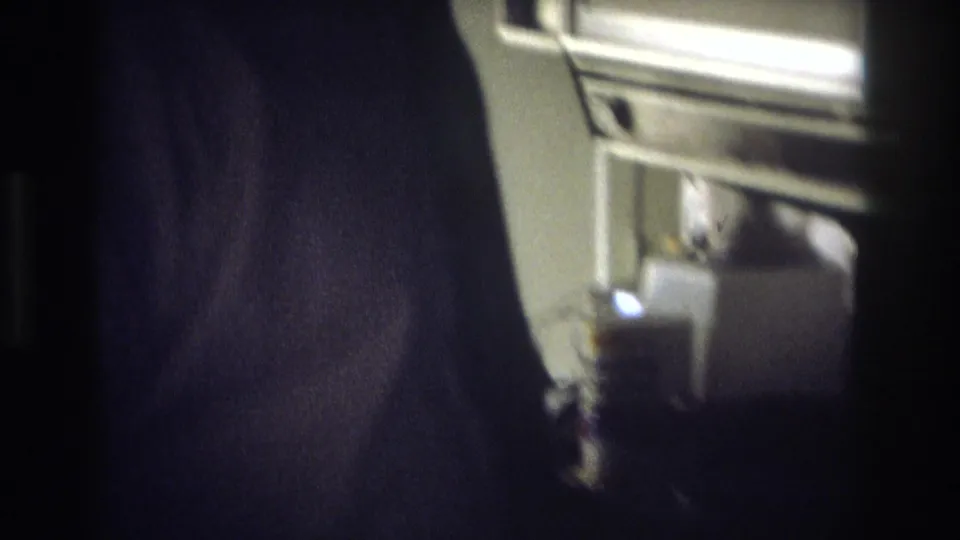 The man moves closer to the stove, with appliance controls and a bright kitchen surface visible in the grainy 8mm frame.