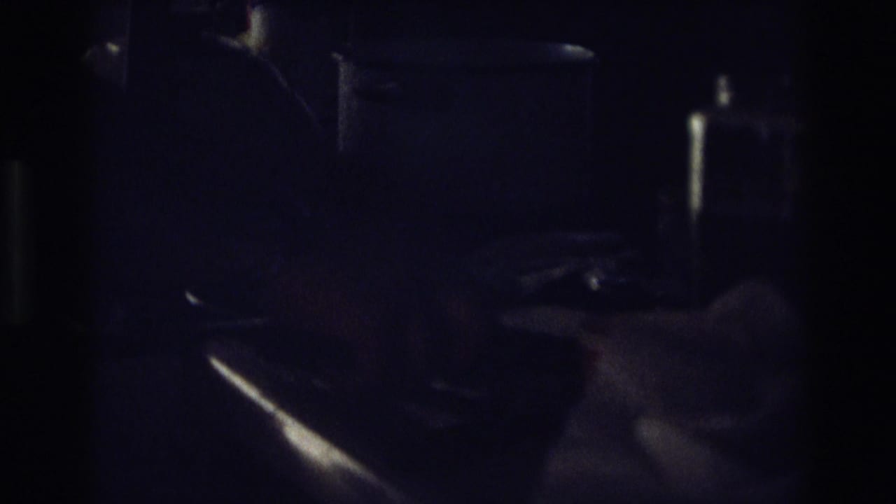 A hand holds a knife near bread in a low-lit kitchen close-up.