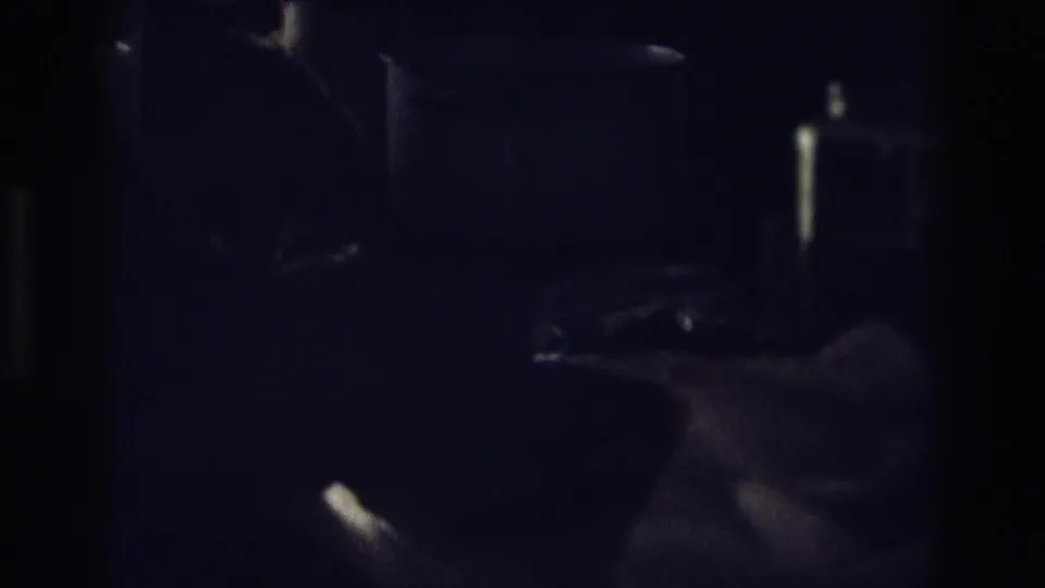 The low-light home-movie frame shows bread, a knife, and a nearby hand on a dark kitchen work surface.