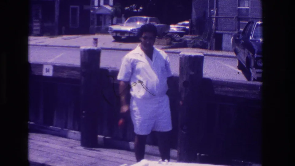 Ocean City, New Jersey home-movie frame showing a man in white shorts on the boardwalk holding a small red object.