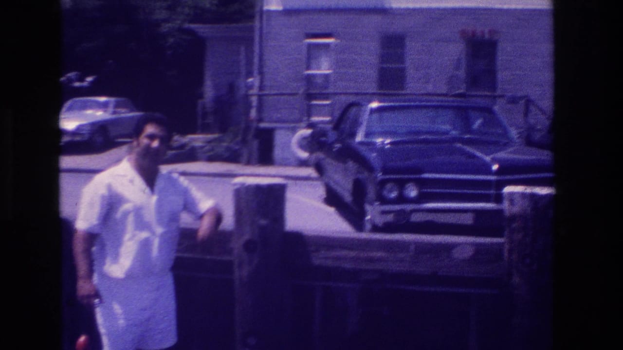 Ocean City, New Jersey home-movie frame showing a man in white by a dock, with a dark sedan and BAIT building in the background.