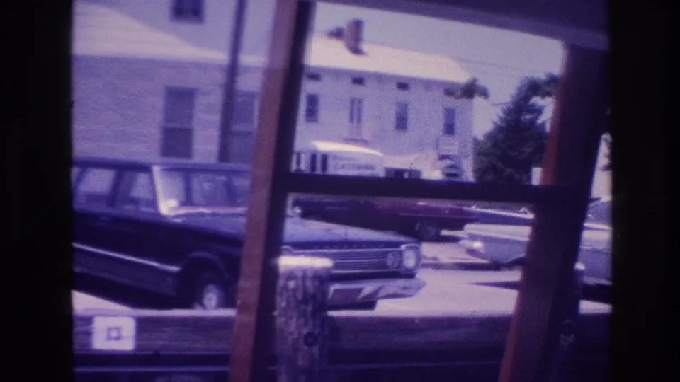 1968 Ocean City waterfront frame with a station wagon, dock posts, parked cars, and a partial building sign in soft 8mm color.
