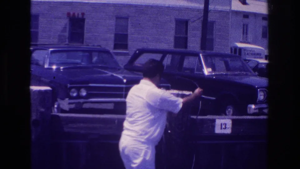 1968 Ocean City frame showing a man in white handling equipment beside parked classic cars and a station wagon.