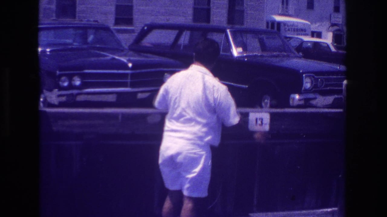 Man seen from behind near a pier rail with classic cars and a catering van sign in the background.