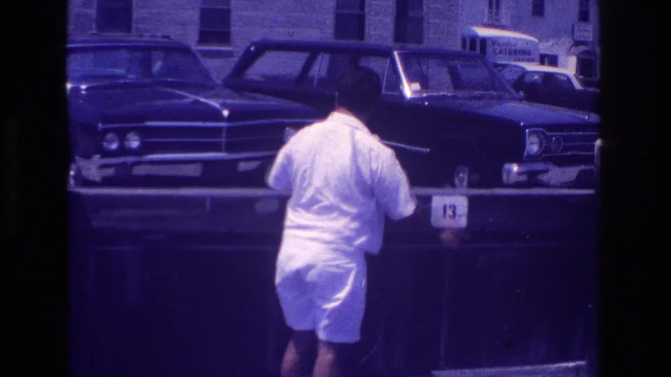 The man is viewed from behind near the pier rail in Ocean City, with 1960s cars and a visible catering sign across the street.