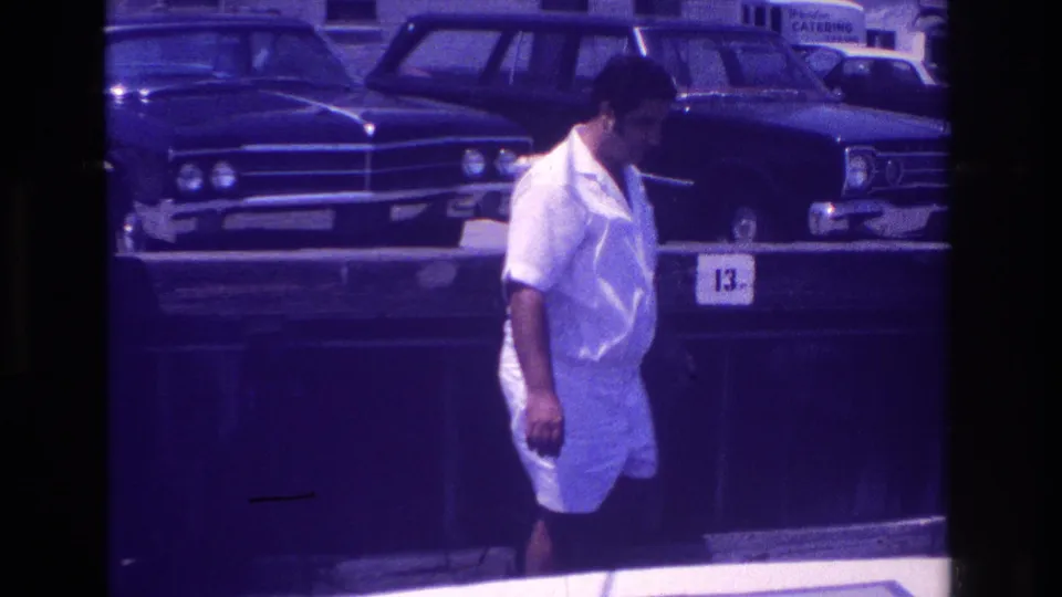 A man in white summer clothes moves along the Ocean City pier edge near a number 13 marker, with classic cars in the background.