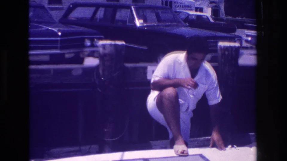 In the final frame, the man crouches beside a wooden pier post near the rail, with 1960s parked cars and street buildings behind him.