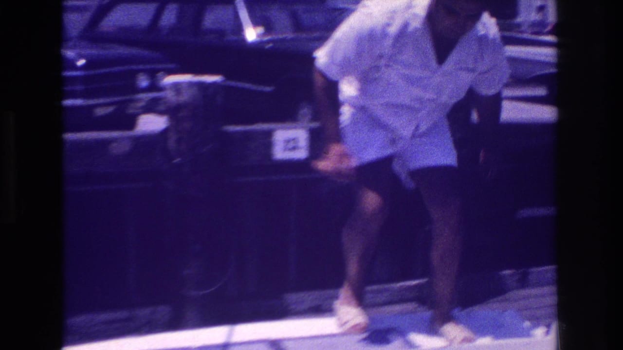 1968 Ocean City, New Jersey home-movie frame showing a man bending near a dock, with parked late-1960s cars and marina equipment behind him.