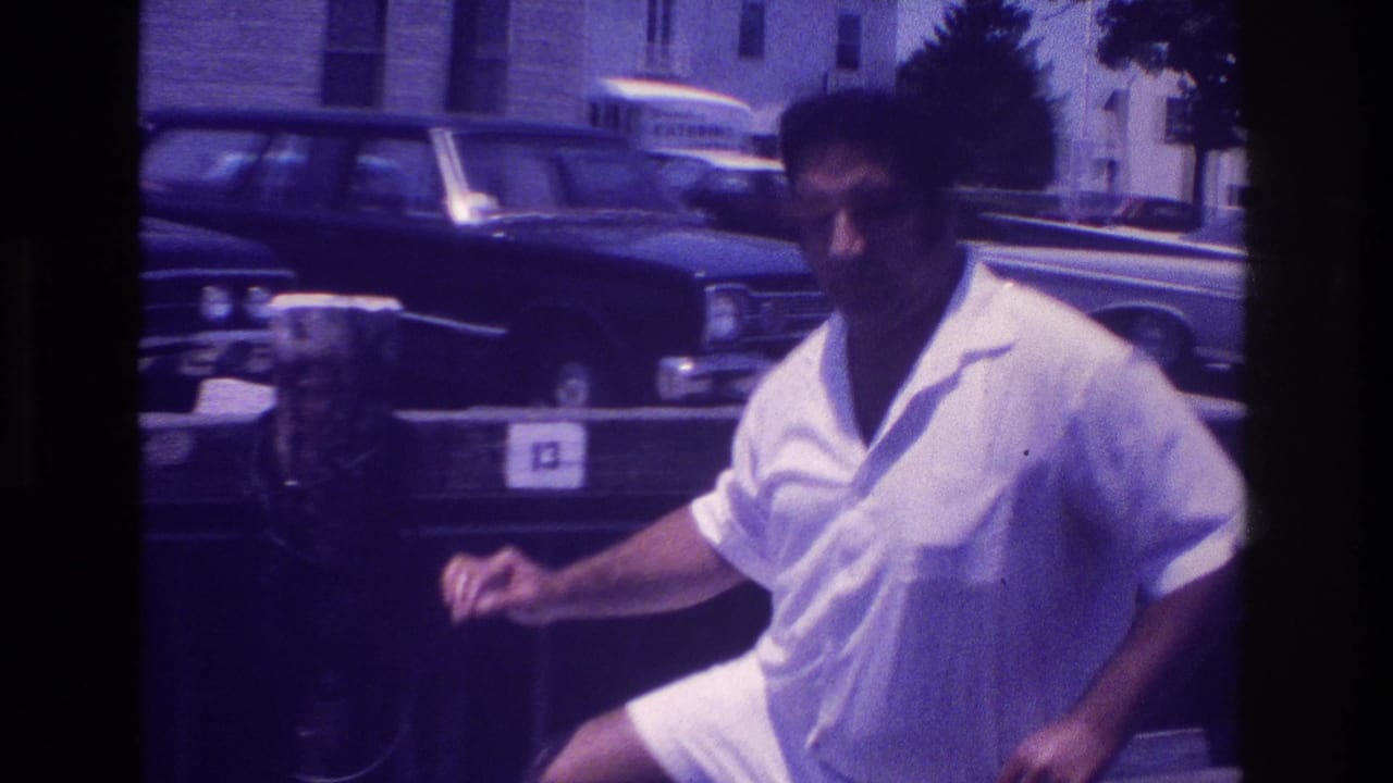Man in white shirt and shorts walking beside marina posts with cars in the background.
