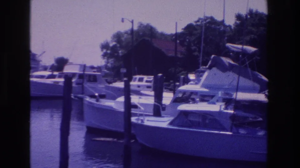 1968 Ocean City, New Jersey frame showing a moored cabin boat at a marina, with dock posts, water, trees, and low shore buildings beyond.