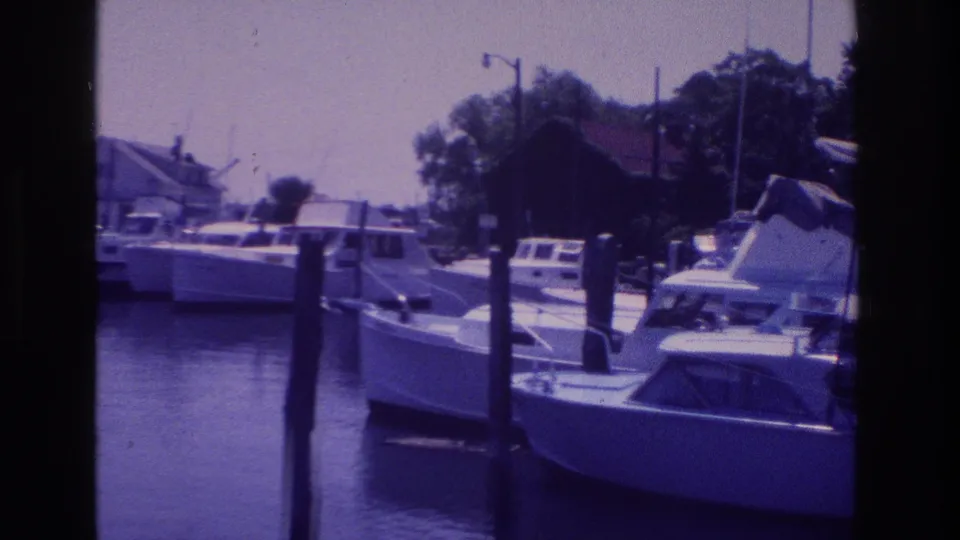 1968 Ocean City, New Jersey home-movie frame of small boats tied near wooden pilings along a quiet marina.