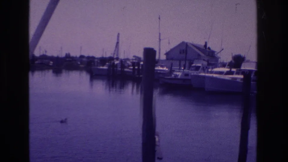 Wide 1968 Ocean City marina frame showing boats, dock pilings, reflections, and a small duck crossing the bay foreground.