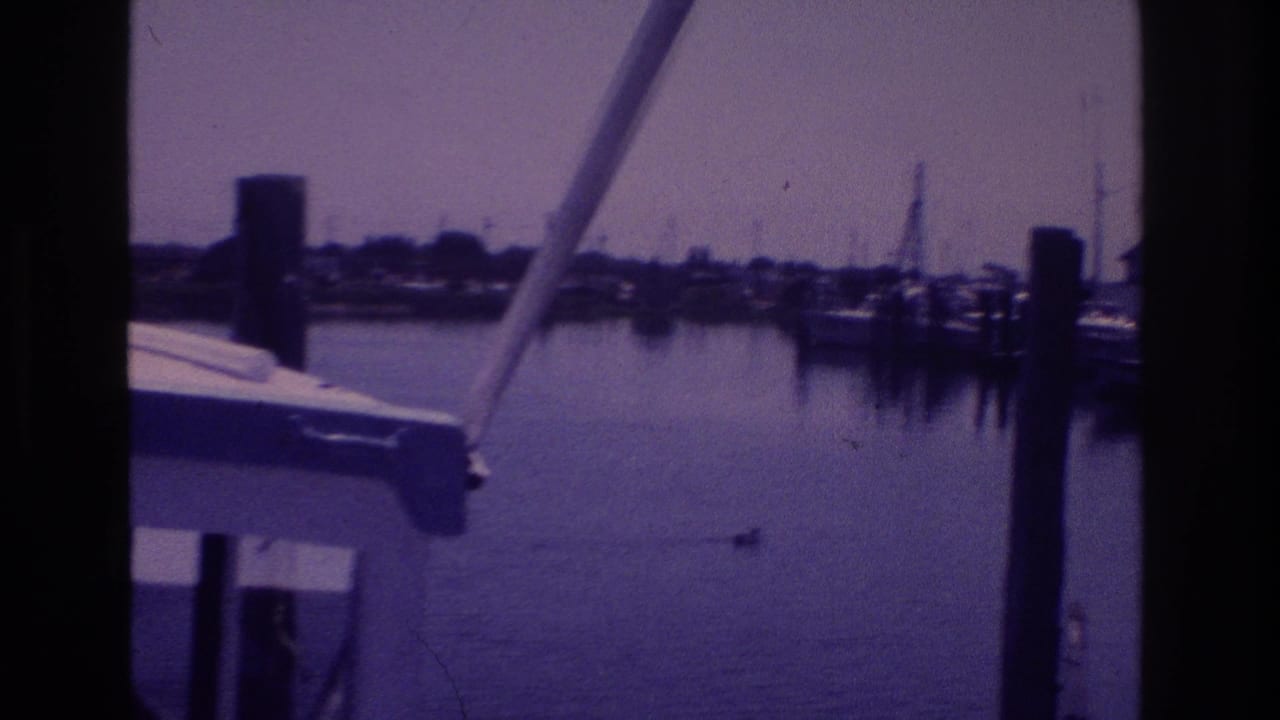 1968 Ocean City harbor view framed by a boat structure, with calm water, dock pilings, and shoreline beyond.