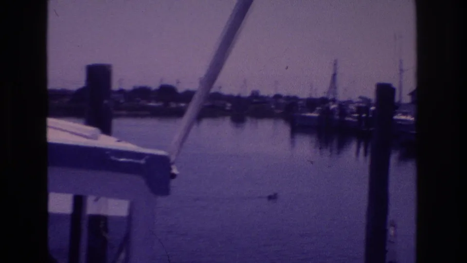 1968 Ocean City harbor view framed by a boat structure, with calm water, dock pilings, and shoreline beyond.
