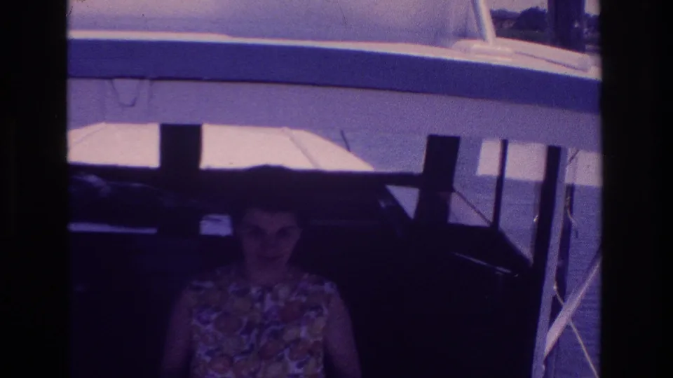 Adult woman in a floral sleeveless dress smiles toward the camera from a boat cabin in the 1968 Ocean City harbor scene.
