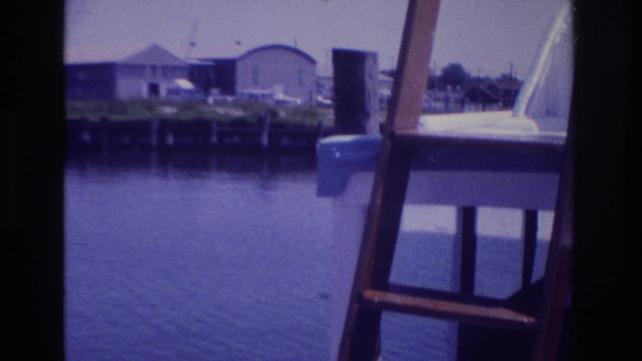 1968 Ocean City, New Jersey boat view with a wooden ladder in the foreground, dock pilings, calm water, and low waterfront buildings.