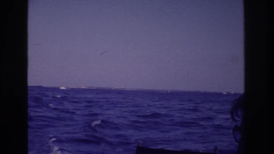 Blue-white ocean swells and a distant low shoreline appear through the boat structure in this 1968 Ocean City home-movie view.