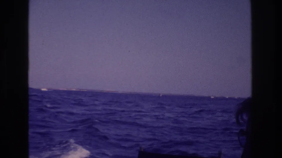 The boat-mounted camera catches rough water, whitecaps, distant land, and a partial silhouetted figure or boat edge in the Ocean City footage.