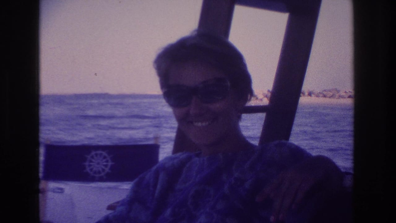 1968 Ocean City home-movie frame showing a woman in sunglasses smiling on a boat, with water and distant shoreline in the background.