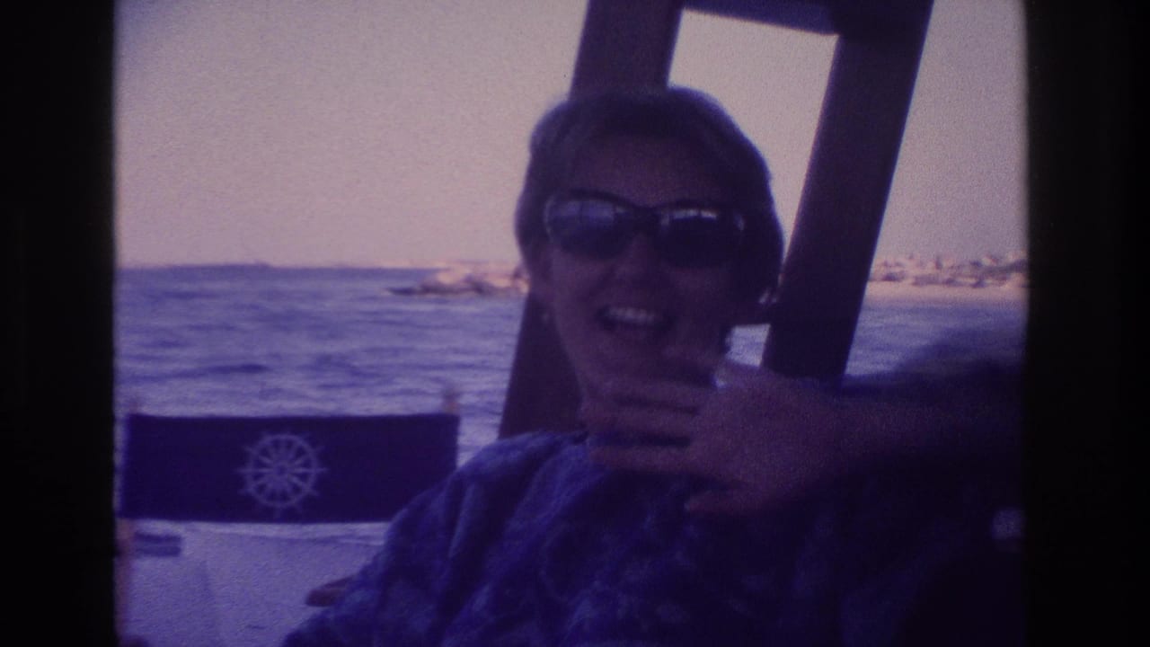 1968 Ocean City frame of a woman in sunglasses laughing on a boat, partly covering her face with one hand.
