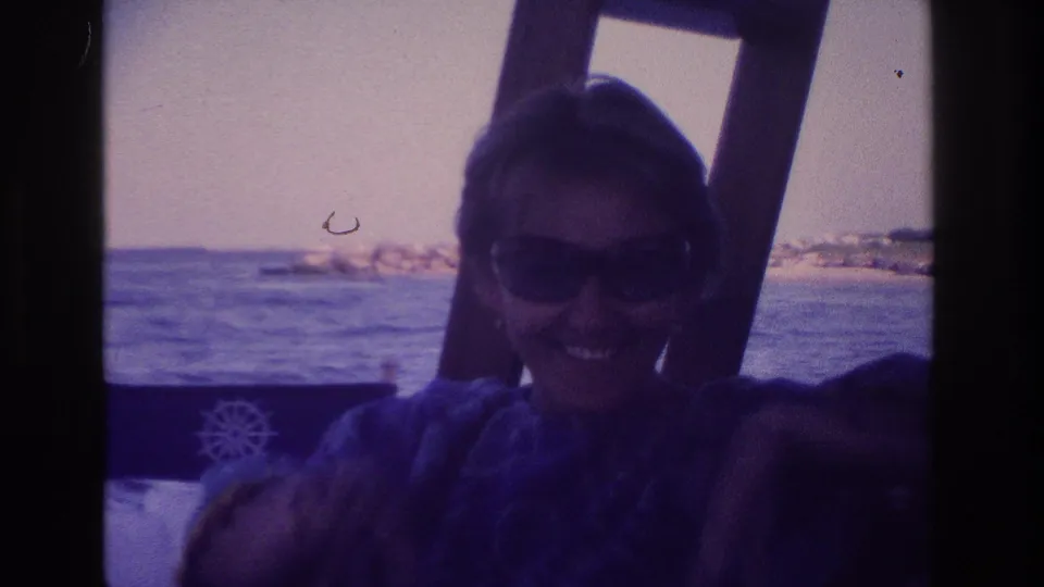 1968 Ocean City home-movie frame showing a woman in sunglasses leaning toward the camera on a boat with ocean water behind her.