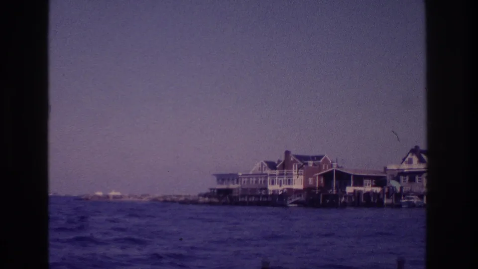 1968 Ocean City boat-trip frame with seaside houses, low shoreline, and visible 8mm film borders.