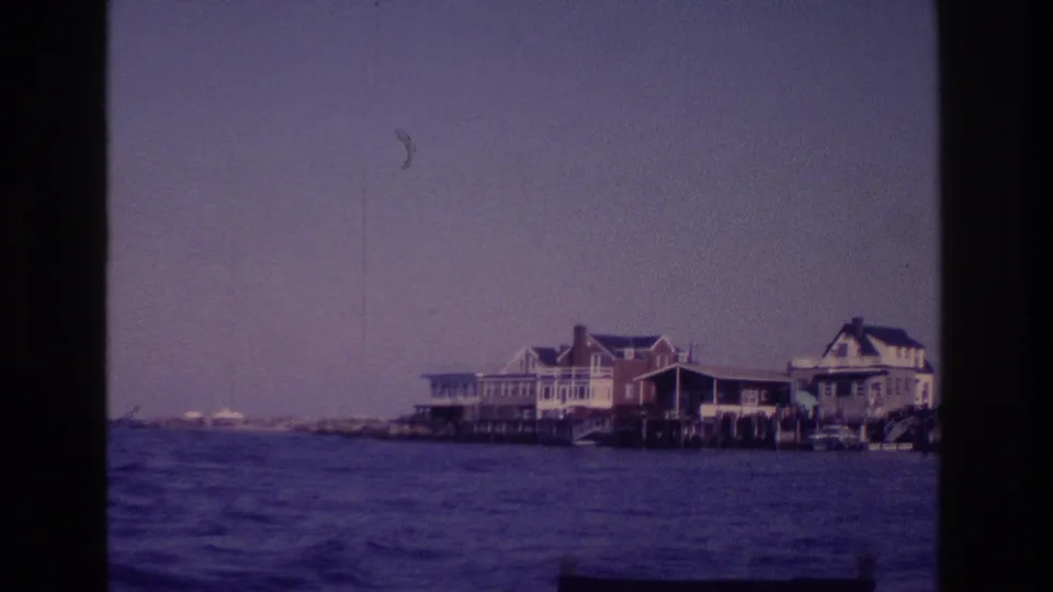 Ocean City, New Jersey shoreline houses viewed from a boat, with grainy 8mm texture and purple-blue color cast.