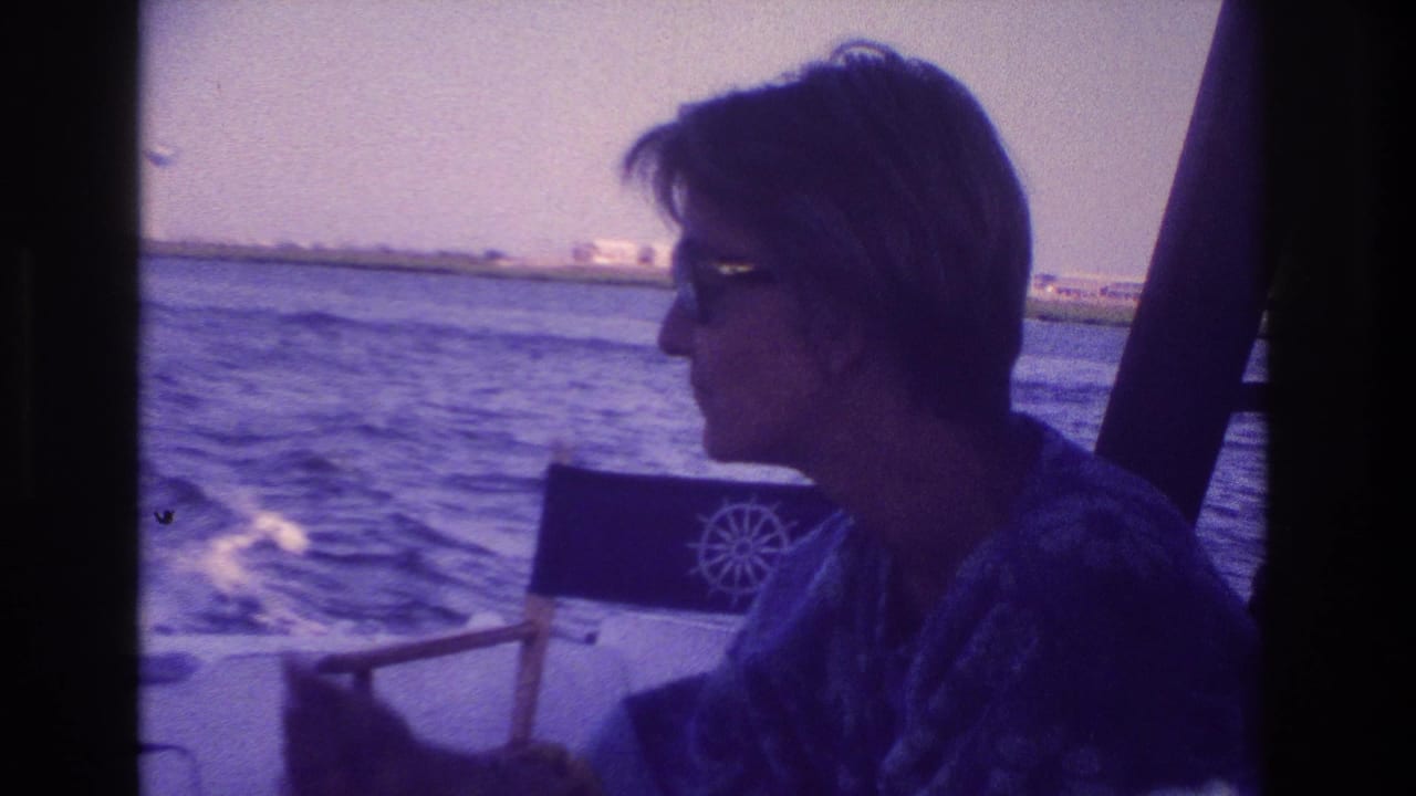 Profile view of a woman on a boat beside a chair as choppy water trails behind.