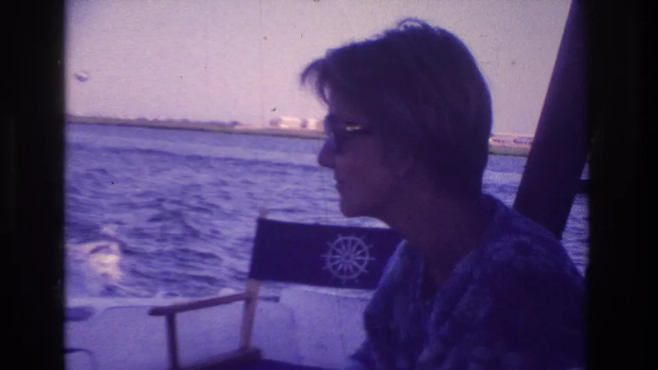 The woman remains seated in profile on the Ocean City boat, with purple-blue 8mm color, a chair behind her, and water filling the background.