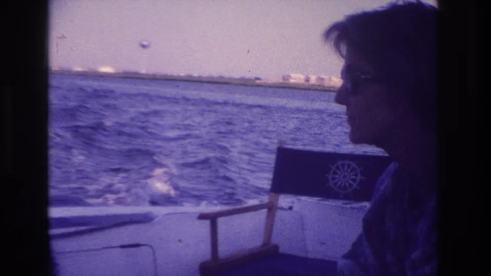At the end of the clip, the woman is partly cropped and shadowed while the boat chair, wake, open water, and Ocean City shoreline remain visible.