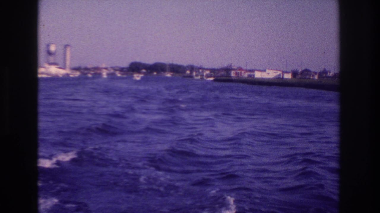 1968 Ocean City, New Jersey 8mm view from a moving boat, with dark wake, rippled water, shoreline buildings, and a water tower in the distance.