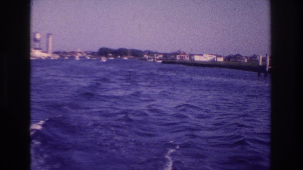Moving-boat view over rough blue water toward the Ocean City shoreline, with waterfront buildings and a tall water tower under a hazy sky.