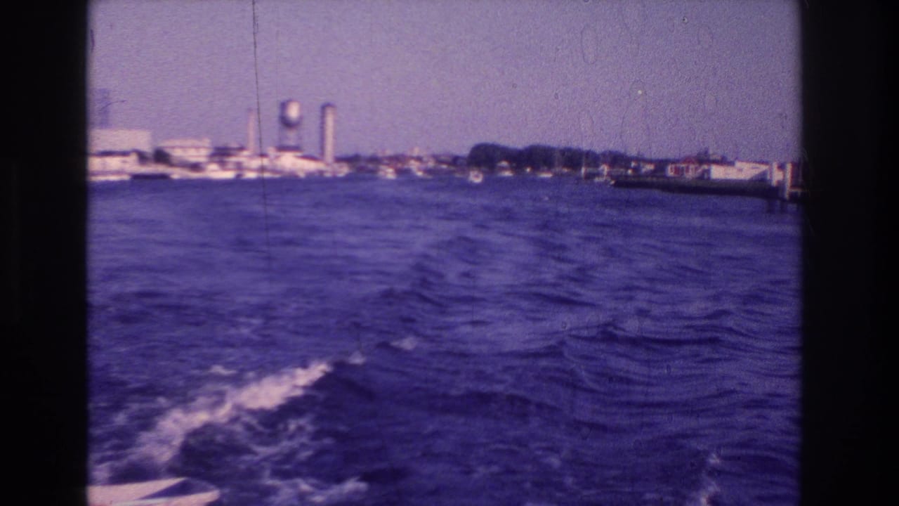 1968 Ocean City, New Jersey home-movie frame showing rippled water, boat wake, docks, and a distant water tower.